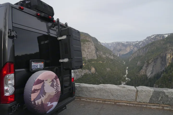 RV rental camper van with gear overlooks Yosemite Valley. Stunning mountain views, river, and waterfall for #vanlife travel.. Winnebago Solis 2022
