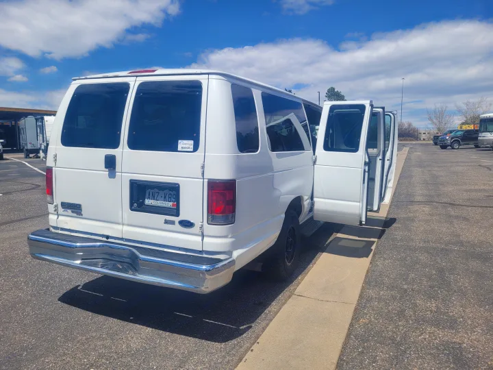 White Ford E-350 van, an ideal rv rental, is seen with its side doors open in a large parking lot alongside other RVs.. Ford Ford E350 2009