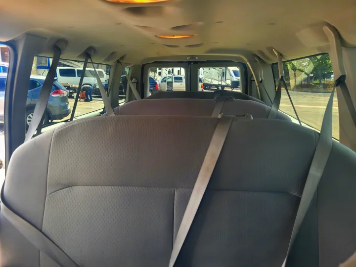 View from inside an RV rental van showing three rows of grey seats and seatbelts, with RVs outside in a sunny parking lot.. Ford Ford E350 2009