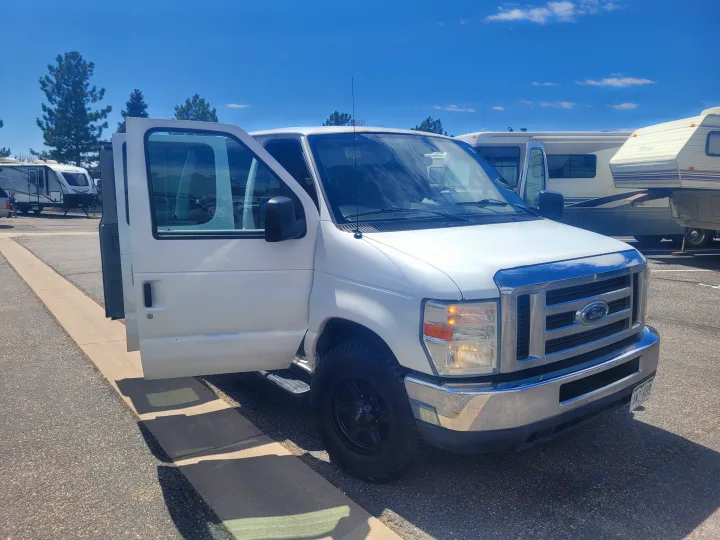 Bright white Ford van with open doors parked among various RVs under blue skies. Ideal rv rental for adventure travel.. Ford Ford E350 2009