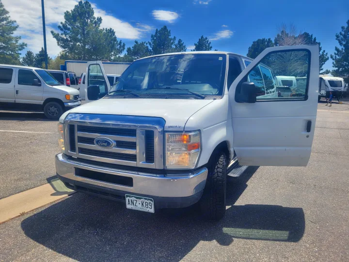 White Ford van with open door, parked at an RV rental lot with travel trailers. Colorado license plate ANZ-K89.. Ford Ford E350 2009