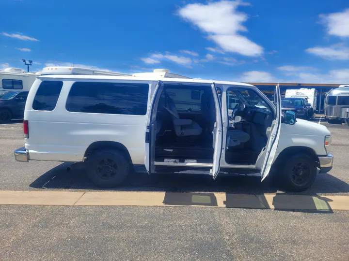 White passenger van with all side doors open, parked at an RV rental facility among other RVs under a blue sky.. Ford Ford E350 2009