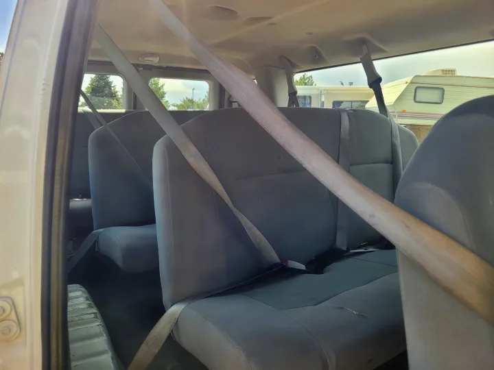 View from inside a passenger van with grey seats and seatbelts, offering a glimpse of an RV rental in the background.. Ford Ford E350 2009