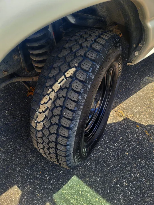 Front wheel of an RV rental, featuring a rugged all-terrain tire and visible coil spring suspension components.. Ford Ford E350 2009