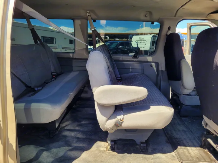 Interior of an RV rental van, showing spacious grey passenger seats. Through windows, RVs are parked under a blue sky.. Ford E-350 2007
