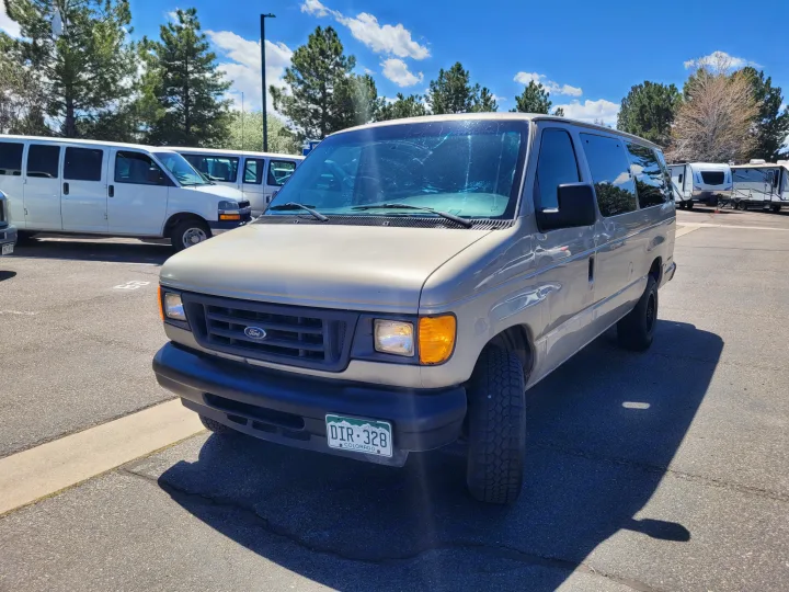 Tan Ford van parked in an RV rental lot on asphalt, with other white vans and travel trailers under a blue sky.. Ford E-350 2007