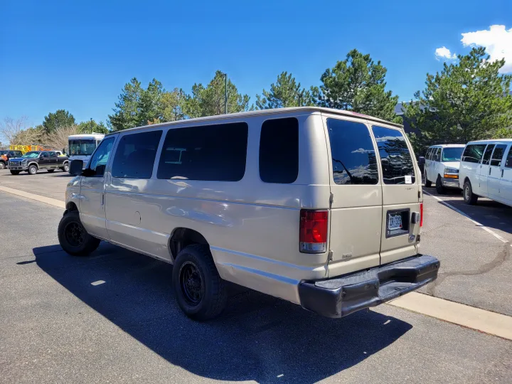 A tan Ford Econoline van, resembling an RV rental, parked on asphalt on a sunny day. Other vans nearby.. Ford E-350 2007
