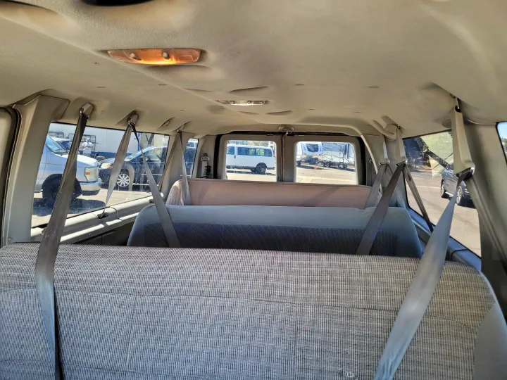 Interior of a passenger van, showing rows of grey fabric seats and hanging seatbelts. An RV rental and other vehicles are visible outside.. Ford E-350 2007