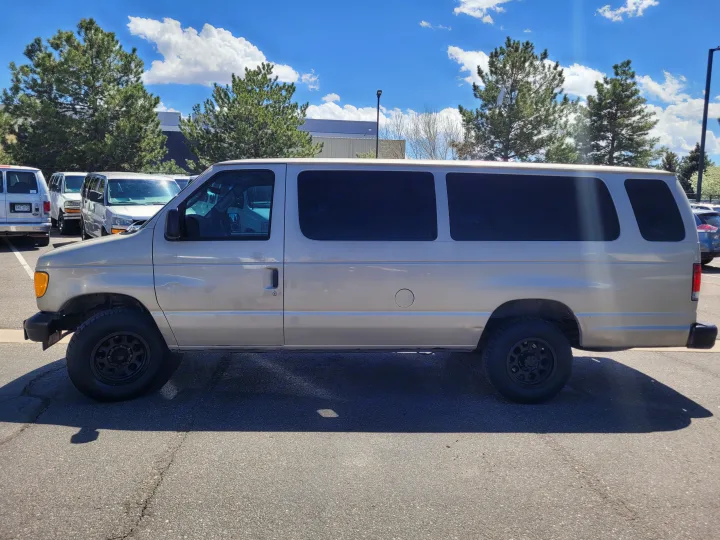 Side view of a light-colored Ford Econoline-style passenger van, perfect as an RV rental, parked on asphalt with trees & sky.. Ford E-350 2007
