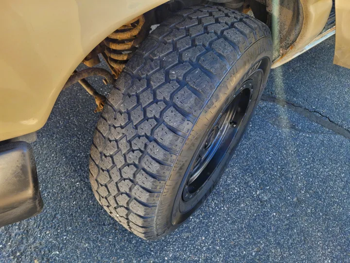 Close-up of an RV rental's front wheel, showcasing its rugged tire tread and visible suspension on asphalt.. Ford E-350 2007