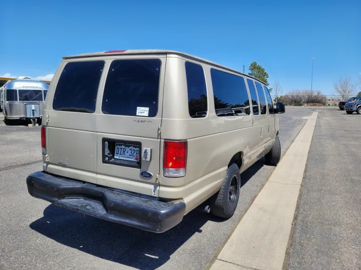 A tan Ford camper van (possible rv rental) is parked near a silver Airstream, ready for adventure.. Ford E-350 2007