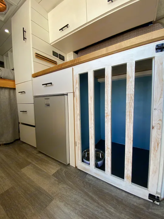 Compact RV rental interior featuring a built-in dog crate, kitchen area with fridge, and storage. Perfect for pet travel.. Ford Transit Custom 2015