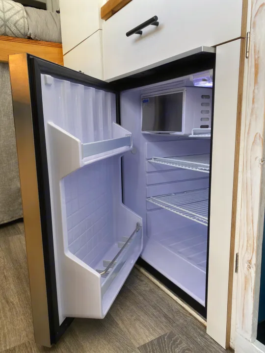 This RV rental features an open, clean compact refrigerator with interior shelves, perfect for your journey.. Ford Transit Custom 2015