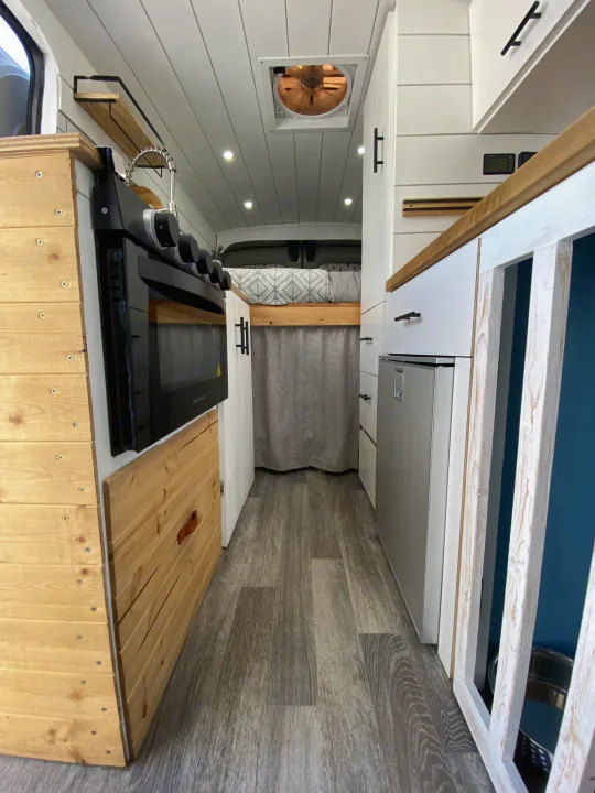 Inside an RV rental: a compact yet functional camper van kitchen with stove, refrigerator, and cozy sleeping area.. Ford Transit Custom 2015