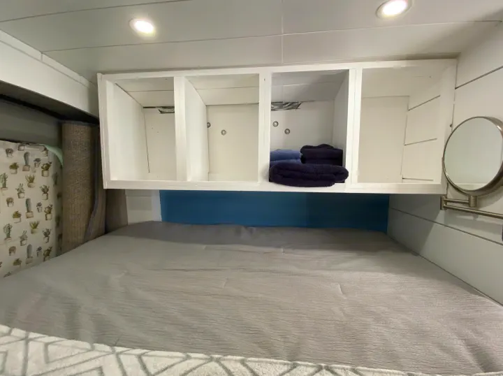 Inside an RV rental: a cozy bed, white storage cubbies with folded towels, and a blue accent wall. Compact and functional space.. Ford Transit Custom 2015
