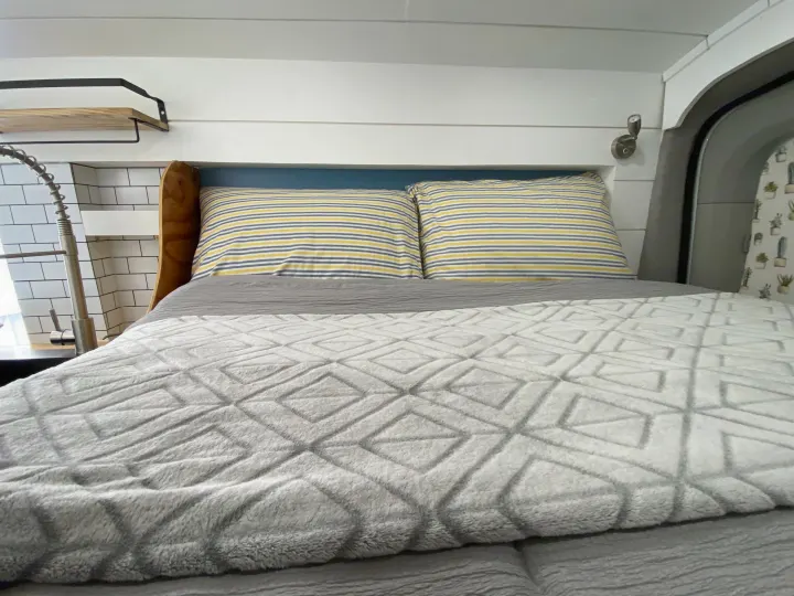 Cozy RV rental interior: A comfy bed with striped pillows, adjacent to a functional kitchen sink & shiplap walls.. Ford Transit Custom 2015