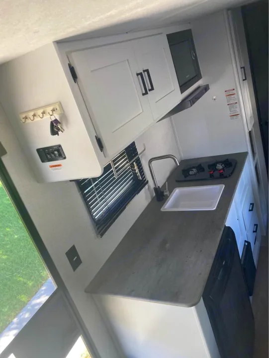 An rv rental's compact kitchen featuring a sink, two-burner stovetop, microwave, and under-counter fridge.. Keystone RV Hideout 2022