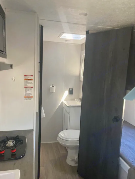 RV rental interior: compact kitchen with stove, sink, and an RV bathroom with toilet, vanity, and skylight.. Keystone RV Hideout 2022