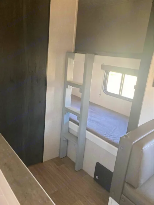 RV rental interior: bunk beds with ladder, window, and light wood flooring. A compact sleeping area.. Keystone RV Hideout 2022