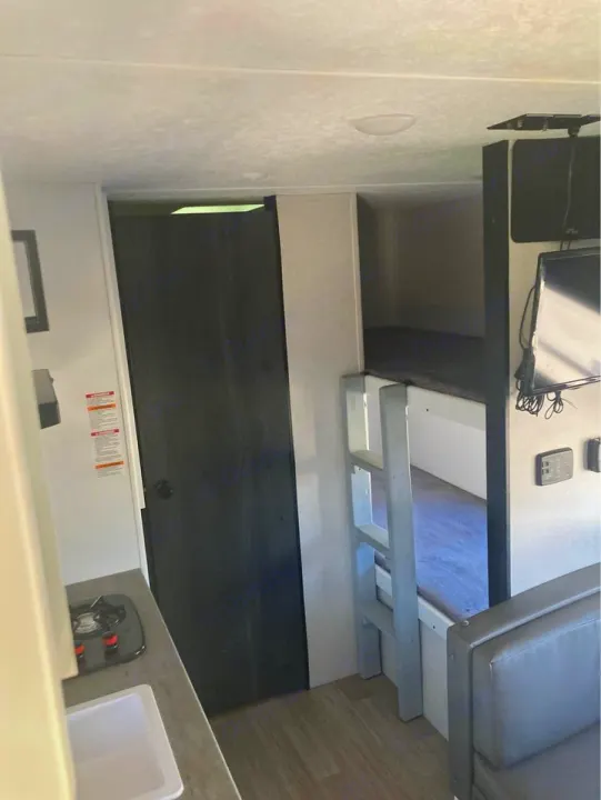 This RV rental's interior shows bunk beds, a compact kitchen with a sink and stove, and a seating area with a TV.. Keystone RV Hideout 2022