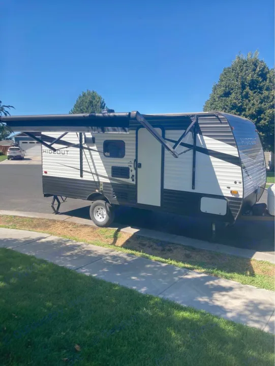 A white and black Hideout travel trailer is parked with its awning extended, ready for your next RV rental.. Keystone RV Hideout 2022