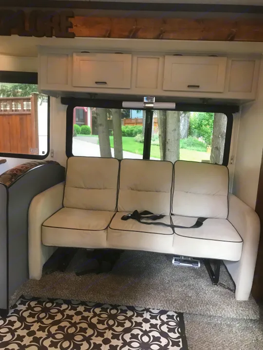 Comfortable seating in this RV rental, featuring a three-seat couch, overhead cabinets, and large windows with outdoor views.. Other Other 2008