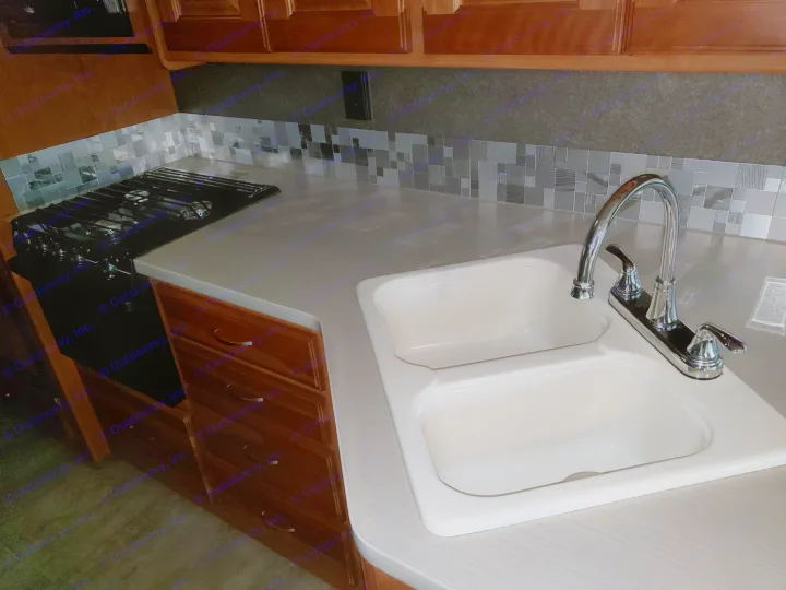 This modern RV rental kitchen features a gas stove, double sink, and sleek grey countertops with a mosaic backsplash.. Winnebago Vista 2017