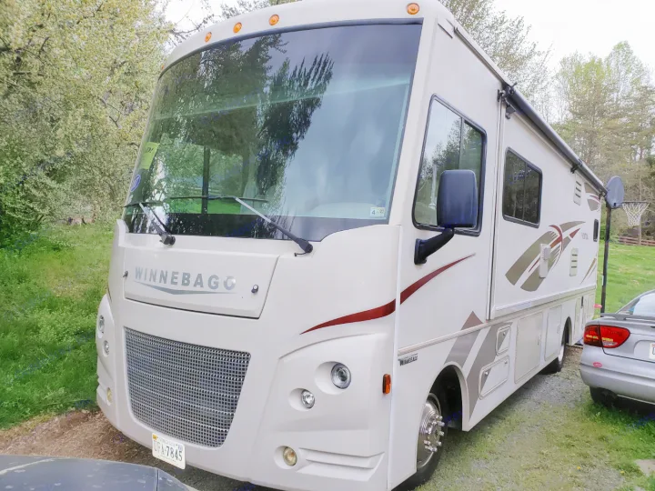 Cream-colored Winnebago RV, perfect for an rv rental, is parked outdoors. Its large front, grille, and windshield are prominent.. Winnebago Vista 2017