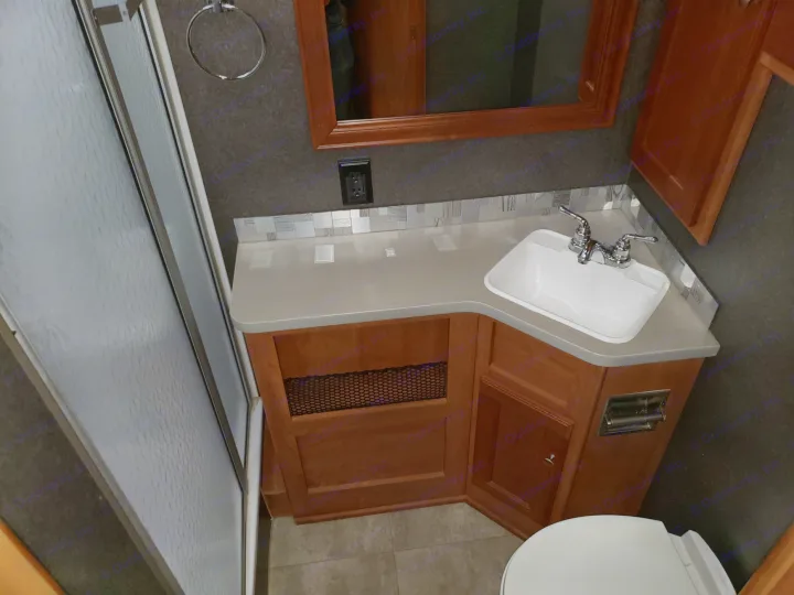 Compact RV rental bathroom featuring a white sink, wood vanity, toilet, and shower door.. Winnebago Vista 2017