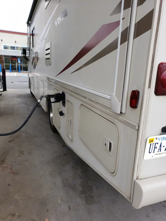 Beige RV rental motorhome fueling up at a gas station, seen from the side with the nozzle inserted.. Winnebago Vista 2017