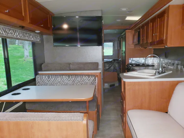 RV rental interior showcasing a dinette, wall-mounted TV, and kitchen with sink and stove.. Winnebago Vista 2017