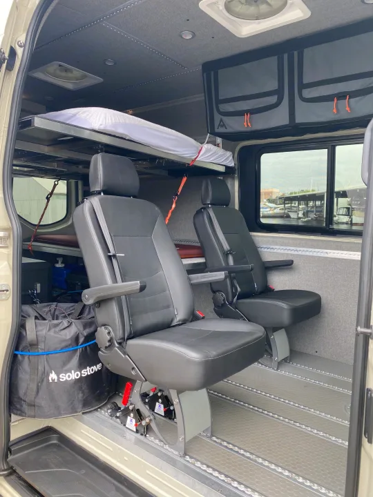 RV rental interior featuring flexible passenger seats, overhead bunk bed, storage, and a marina view. Ideal for travelers.. Mercedes-Benz Sprinter 2023
