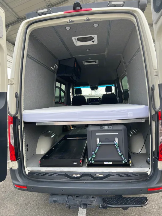 RV rental van interior: custom setup with vertically stowed bed, secured fridge, and modular track system.. Mercedes-Benz Sprinter 2023