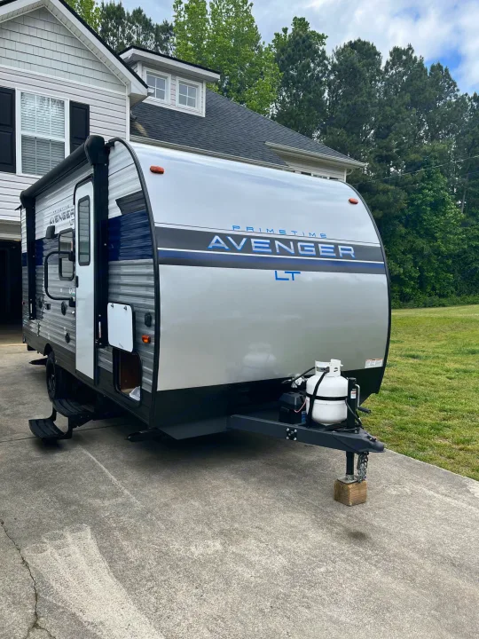 This sleek Prime Time Avenger LT travel trailer, perfect for an rv rental, is parked in a driveway, ready for adventure.. Avenger LT 2022