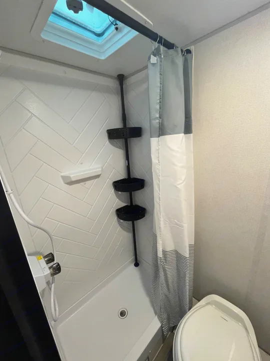 RV rental interior: compact bathroom with a white herringbone shower, corner caddy, toilet, and skylight.. Avenger LT 2022