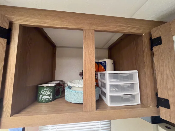 RV rental overhead cabinet showing camping mugs, paper plates, organized utensils, and paper towels. Convenient storage.. Avenger LT 2022