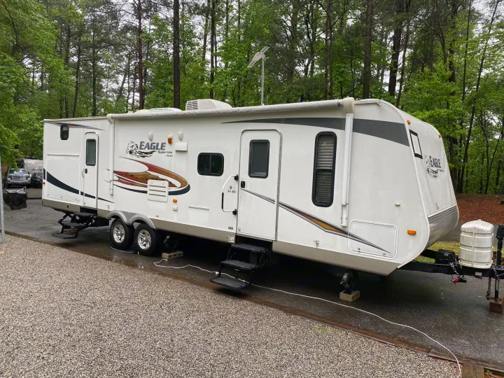 Spacious Jayco Eagle travel trailer RV rental, white with brown accents, parked at a wooded campground.. Jayco Eagle Super Lite 2010