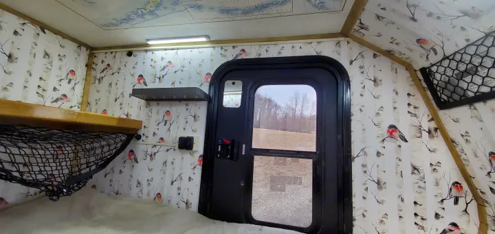 Cozy RV rental interior featuring a bed, storage net, and birch tree/bird decor. View out the door to fields.. Haulmark Homesteader 2005