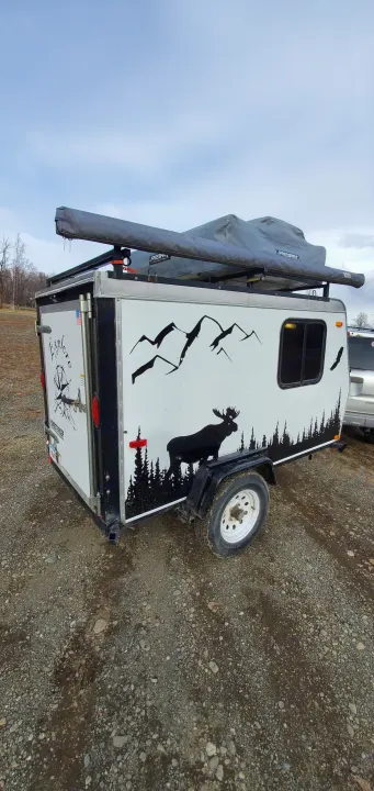 Compact adventure RV rental: A white camping trailer with nature decals and rooftop tent, parked on gravel, perfect for outdoor exploration.. Haulmark Homesteader 2005