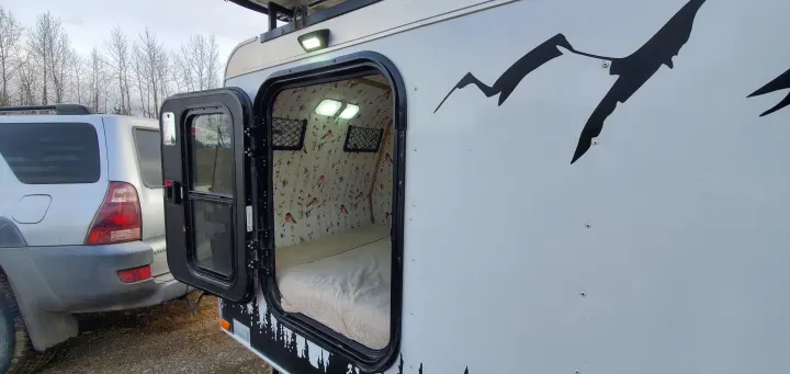 Cozy RV rental with open door revealing a bed, birch tree wallpaper, and lights inside. Ready for your next adventure.. Haulmark Homesteader 2005