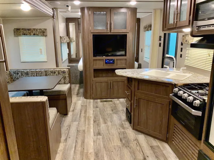 Spacious RV rental interior featuring a full kitchen, dinette, entertainment center, and a glimpse of the bedroom.. Keystone RV Hideout LHS 2019