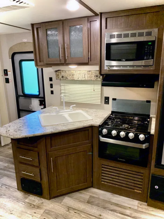Modern RV rental kitchen with sink, stove, microwave, and ample cabinets, ideal for travel comfort.. Keystone RV Hideout LHS 2019