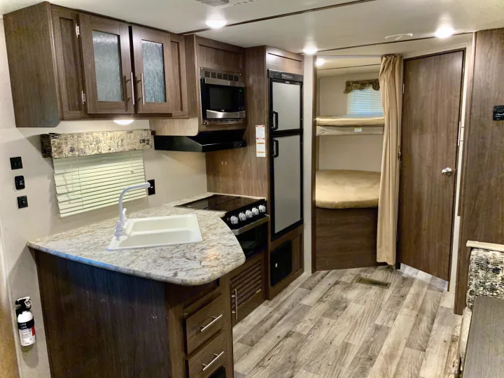 Experience comfort in this RV rental: a compact kitchen with appliances, sink, and counter, leading to a bunk bed area.. Keystone RV Hideout LHS 2019