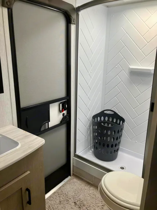 RV rental bathroom: compact design with shower, toilet, sink, and a screen door for ventilation. Includes a laundry basket.. Forest River Salem Cruise Lite 2023
