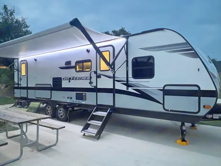 Your perfect RV rental: Jay Feather travel trailer illuminated at dusk, with an extended awning, steps, and picnic table.. Jayco Jay Feather 2022