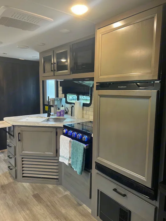 Modern rv rental kitchen with sleek gray cabinets, Furrion appliances (fridge, microwave, stove), and sink. Light wood flooring.. Jayco Jay Feather 2022