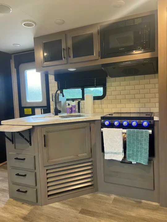 Fully equipped rv rental kitchen featuring a modern microwave, stove, sink, and ample storage.. Jayco Jay Feather 2022