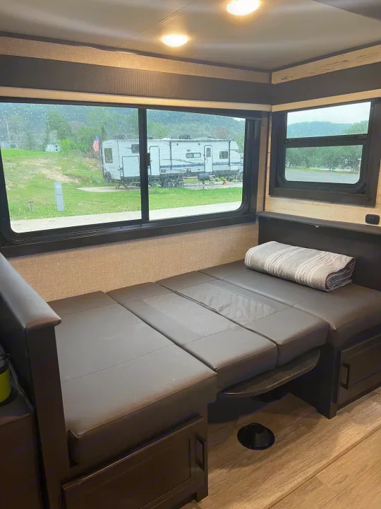 RV rental interior: a dark convertible dinette/sofa overlooks a rainy campground view through large windows.. Jayco Jay Feather 2022