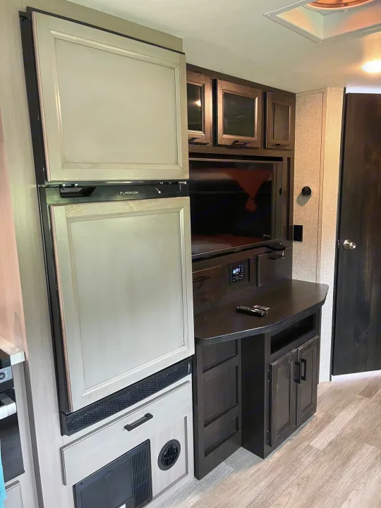 Modern RV rental interior featuring a Furrion fridge, TV entertainment center, and ample storage, ideal for road trips.. Jayco Jay Feather 2022