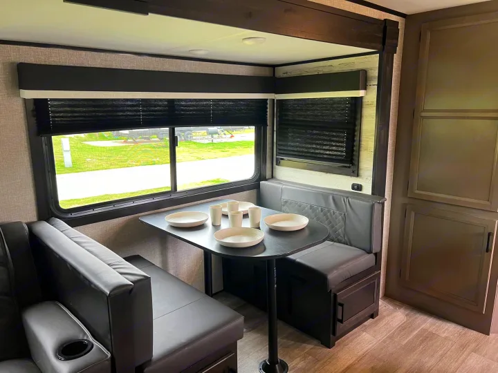 Step inside this inviting RV rental: a cozy dinette with dark upholstered benches, a table set for four, and bright windows.. Jayco Jay Feather 2022